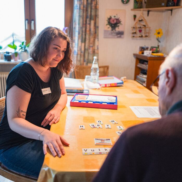 Eine Logopädin sitzt mit einem Herrn am Tisch und spielt ein Gesellschaftsspiel